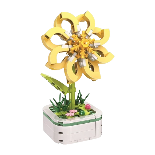 Hier zu sehen ist eine gelbe Jasminblume aus Klemmbausteinen in einem cremeweißen Topf mit abgerundeten Ecken und einer feinen grünen Zierlinie im oberen Segment. Auf der grünen Noppenplatte als Wiese sprießen kleine dunkle Grashalme und zarte rosa Blüten. Aus der Mitte steigt ein grüner Stängel mit einem seitlichen Blatt auf. Darauf sitzt die Hauptblüte aus acht geschwungenen, hellgelben Blütenblättern, die wie offene Schlaufen geformt sind und einen detaillierten gelben Blütenstempel umschließen.